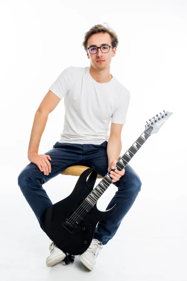 Mann in weißem Shirt mit E-Gitarre sitzt auf Hocker, Teammitglied von danysmusicschool.at - Peter Grupinski